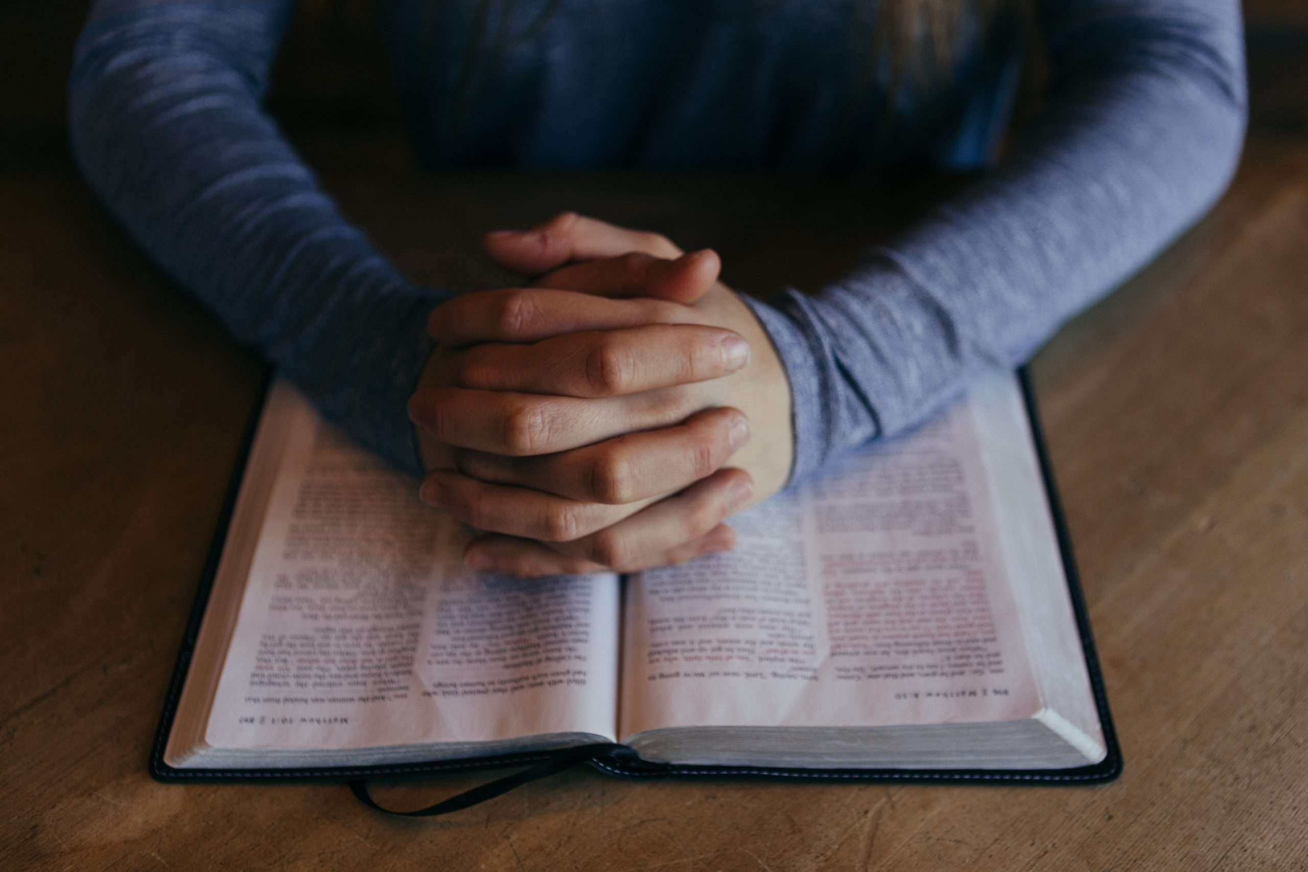 Praying hands on top of a bible